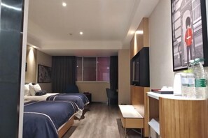 A hotel room with two beds, a desk, a chair, a TV, and a window.