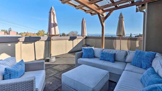 Un espace extérieur aménagé, abrité et doté d’un canapé et d’un pouf, de parasols et d’une structure en forme de pergola.
