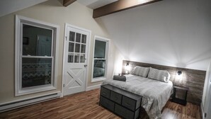 A bedroom with a sloped ceiling, a bed with a headboard, a bench, two windows, and a door.