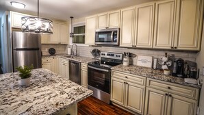 A kitchen with white cabinets, stainless steel appliances, granite countertops, and a hanging light fixture.