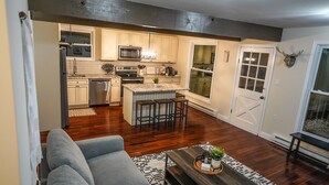 A modern kitchen with wooden cabinets, a central island, and a dining area with bar stools.