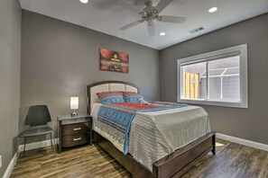 A bedroom with a bed, a nightstand, a chair, a ceiling fan, a window, and a painting on the wall.