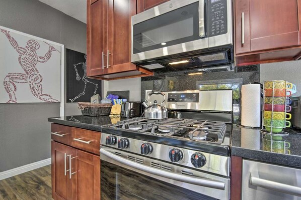 A modern kitchen with stainless steel appliances, wooden cabinets, and a decorative wall piece.
