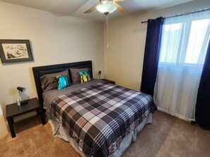 A bedroom with a bed, a nightstand, a ceiling fan, and a window with curtains.