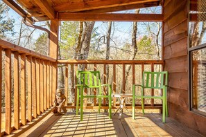 A wooden deck with two green chairs and a table, surrounded by a wooden railing, overlooking a forested area. - Bigfoot Lodge Room Two - Mountain Getaway With Private River Access (Benton)
