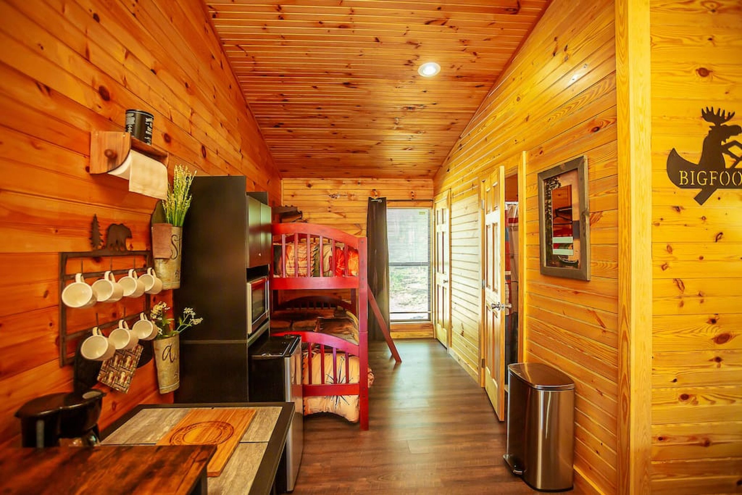 A wooden cabin interior with a kitchen area, a dining table, and a bunk bed.