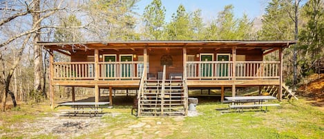 A wooden cabin with a balcony, a fire pit, and picnic tables.