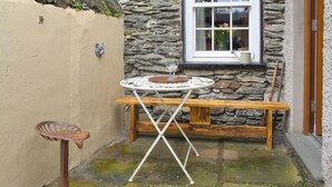 A small outdoor seating area with a stone wall, a wooden bench, and a table with a metal frame.
