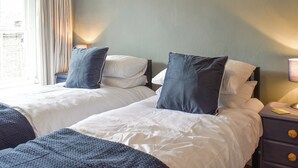 A hotel room with two beds, a nightstand, a lamp, and a window with curtains.