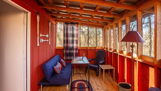 A cozy cabin interior with a blue sofa, a table with a laptop, and a plaid curtain. - Sasquatch Cabin (Benton)