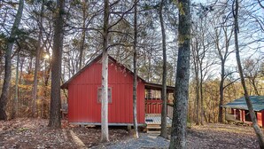A red wooden cabin surrounded by trees, with a wooden deck and a small porch. - Sasquatch Cabin (Benton)