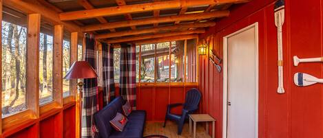 Interior de una cabaña con techo de madera, un sofá, una silla, una mesita y una puerta.
