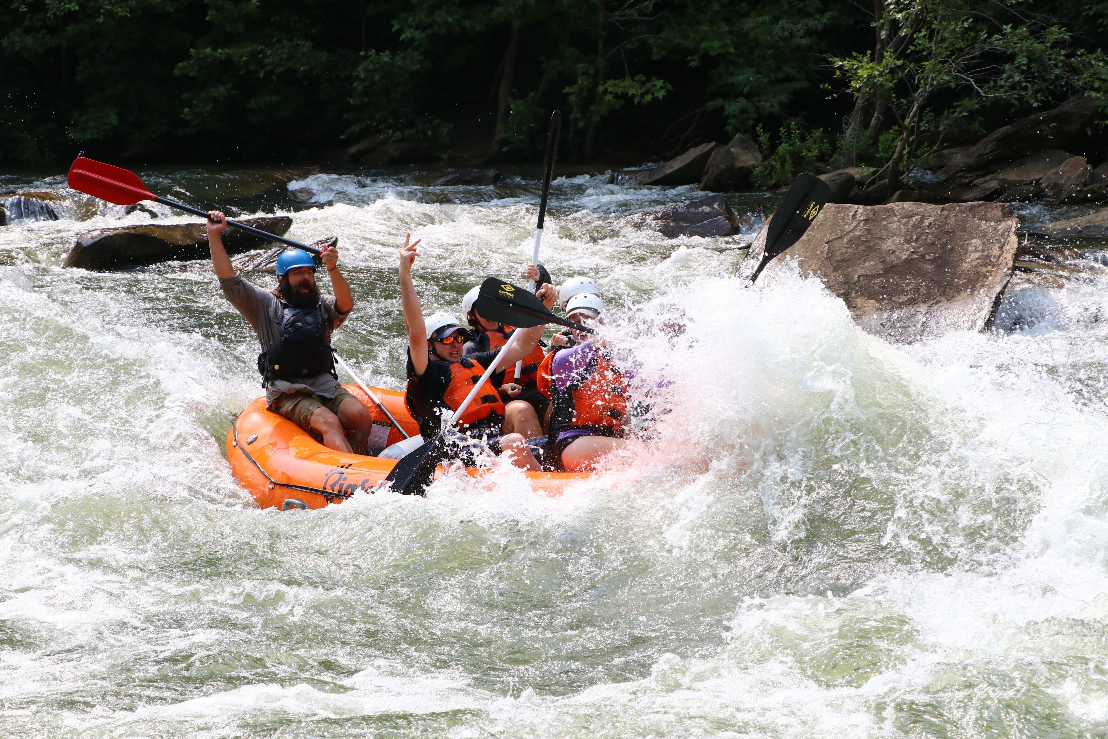 A group of people in an orange raft navigating through a river with rapids.