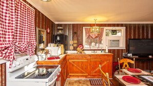 A kitchen with wooden cabinets, a stove, and a dining area with a table set for two. - Sasquatch Cabin (Benton)