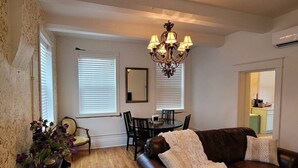 A living room with a brown leather couch, a chandelier, a dining table with chairs, and a kitchen visible through an open doorway. - 502 W Robertson St. Memphis, TX · Converted Historic Jailhouse (Memphis)