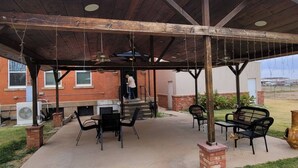 An outdoor patio with a covered seating area, a grill, and a brick building in the background. - 502 W Robertson St. Memphis, TX · Converted Historic Jailhouse (Memphis)