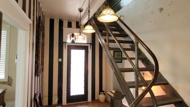 A staircase with a metal railing leading to an upper floor. A door with a frosted glass panel is visible in the background. - 502 W Robertson St. Memphis, TX · Converted Historic Jailhouse (Memphis)