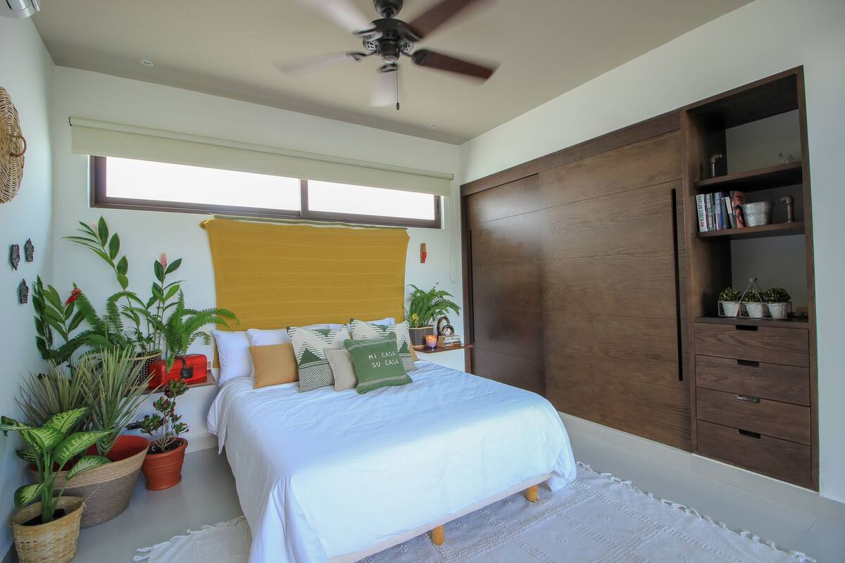Un dormitorio con cama, plantas en macetas, un armario de madera y una ventana con persianas.