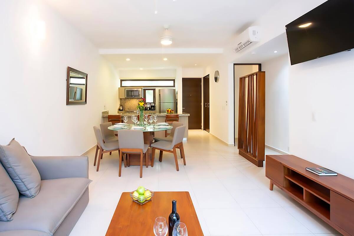 Un salón moderno con sofá, mesa de centro con fruta y vino, y televisor.