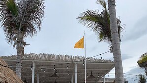 Ett semesterhotell vid stranden med solstolar och parasoller, en byggnad med halmtak och en flagga.