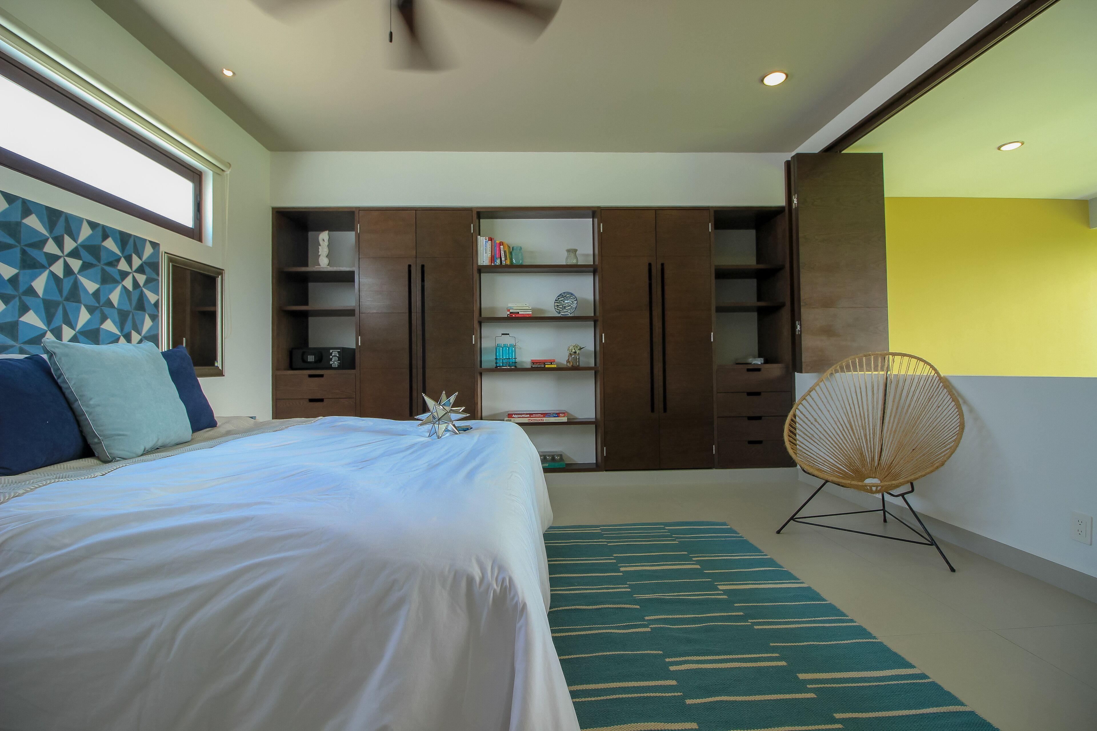 A bedroom with a bed, a bookshelf, a chair, and a geometric wall design.