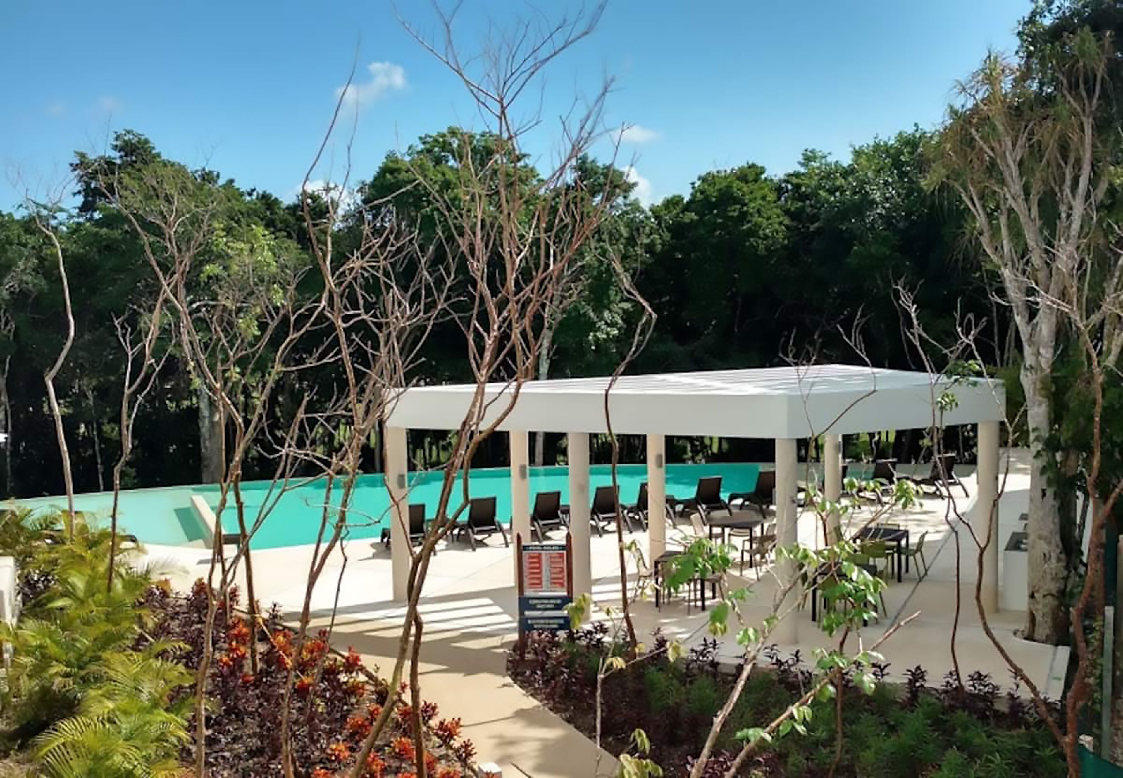 A covered outdoor area with a pool, lounge chairs, and a signboard.