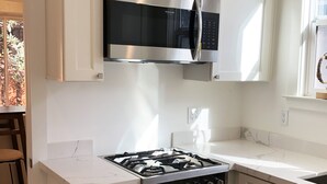 Eine moderne Küche mit weißen Schränken, einer Edelstahl-Dunstabzugshaube, einer eingebauten Mikrowelle, einem Gasherd und einem Backofen.