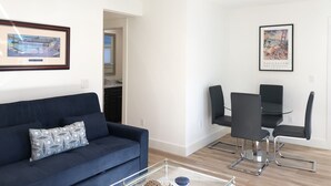 Ein modernes Wohnzimmer mit einem blauen Sofa, einem Glastisch und einem Essbereich mit einem Glastisch sowie schwarzen Stühlen.