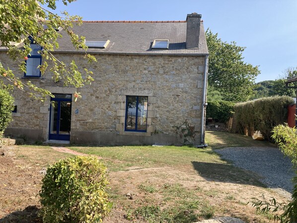 A stone building with a blue door and windows, surrounded by a grassy yard and trees.