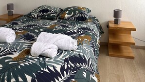 A bedroom with a bed, two bedside tables, a nightstand, a painting, and a staircase. - Warm, modern house 50m from the sea (Trébeurden)