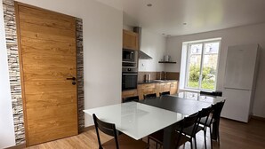 A modern kitchen with a central island, wooden flooring, and a large window providing natural light. - Warm, modern house 50m from the sea (Trébeurden)