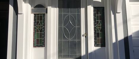 Una entrada frontal con una puerta blanca, dos paneles de vidrio con diseños geométricos y un pequeño escalón que lleva a la puerta.