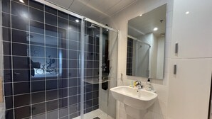 A modern bathroom with a glass shower enclosure, a white sink, and a large mirror. - Apartment in front of Fira Gran Via (Hospitalet de Llobregat - Barcelona)