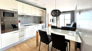 A modern kitchen with white cabinets, stainless steel appliances, and a dining area with a glass table and black chairs. - Apartment in front of Fira Gran Via (Hospitalet de Llobregat - Barcelona)
