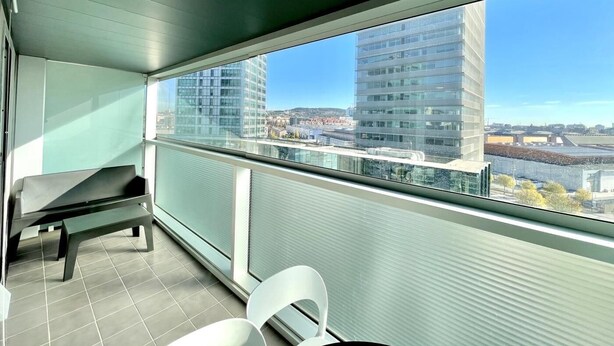 A balcony with a view of modern buildings, a bench, and a chair. - Apartment in front of Fira Gran Via (Hospitalet de Llobregat - Barcelona)