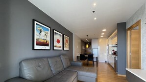 A modern living room with a grey leather sofa, a dining area with a table and chairs, and a kitchen with wooden cabinets and a refrigerator. - Apartment in front of Fira Gran Via (Hospitalet de Llobregat - Barcelona)