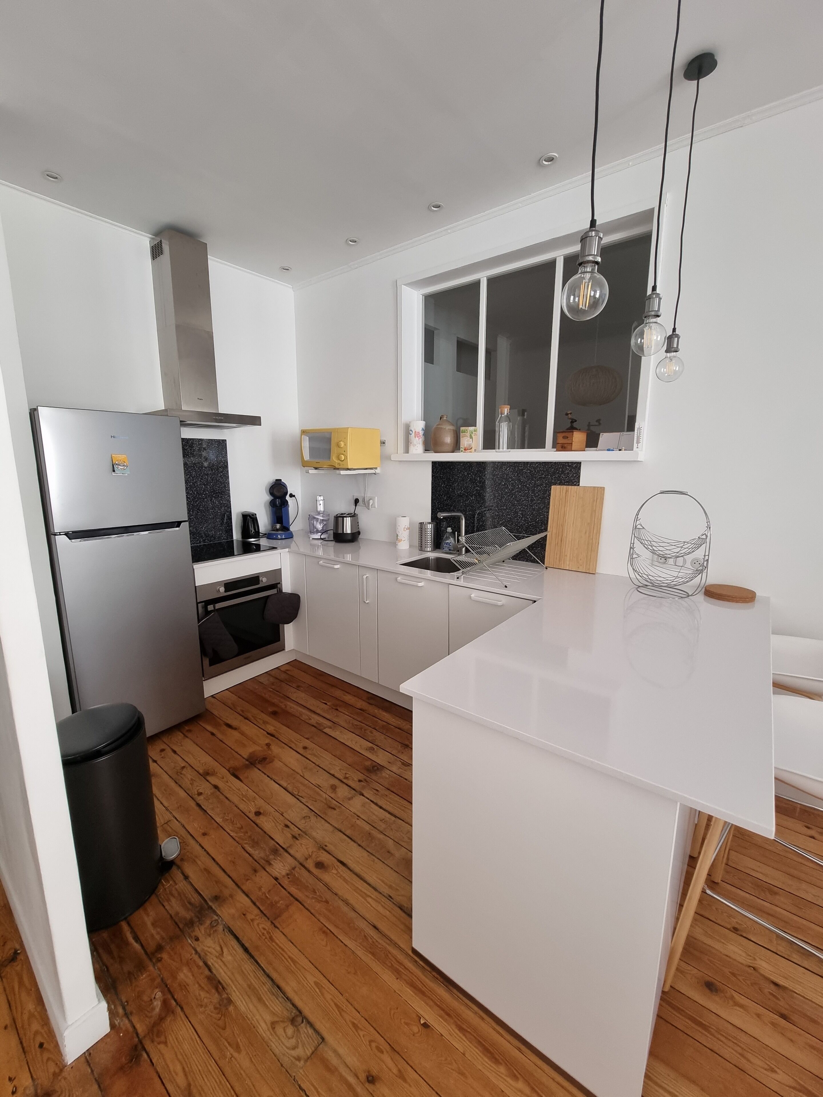 Une cuisine moderne avec des meubles blancs, un réfrigérateur en acier inoxydable, un four encastré et un plancher en bois.
