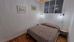 Une chambre avec un plancher en bois, un lit avec une literie à motifs, deux lampes fixées au mur et deux tableaux encadrés.