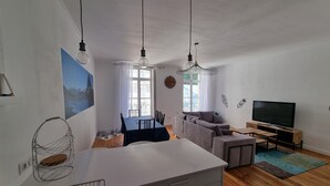 Un salon moderne comprenant un coin repas, un ensemble de canapés, un téléviseur et une grande fenêtre avec des rideaux.