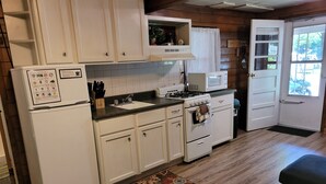 A compact kitchen with white cabinets, a refrigerator, a microwave, and a stove.