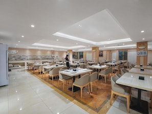 Un comedor amplio con varias mesas y sillas, una persona de pie cerca de la entrada, y una decoración interior moderna y limpia.