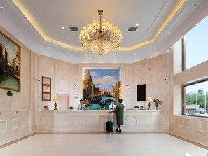 Un vestíbulo de hotel con una recepción, una araña, un gran mural de un paisaje urbano y un ventanal amplio.