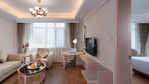 Moderni hotellihuone, jossa on sohva, hedelmillä koristeltu sohvapöytä, työpöytä kannettavalla tietokoneella, televisio ja sänky.