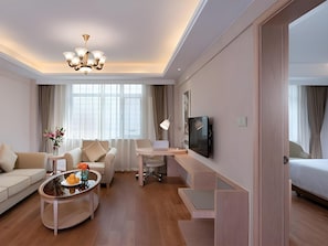 Una habitación de hotel moderna con sofá, una mesita de centro con fruta, escritorio con laptop, televisión y cama.