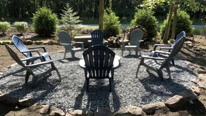 Eine Sitzgelegenheit mit Adirondack-Stühlen und einer Steinkaminfeuerstelle, umgeben von Kies.
