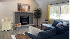 Ein Wohnzimmer mit Kamin, einer Couch, einem Couchtisch und einem Fenster mit Blick auf Bäume.