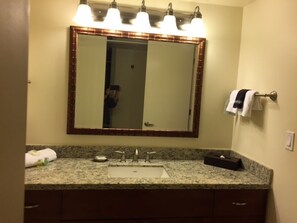 A bathroom with a granite countertop, a sink, a mirror with lights, and a towel rack.