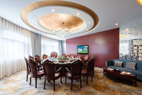 A dining area with a round table, chairs, and a chandelier. There is a sofa and a painting on the wall. - Ausotel Hotel (Bijie)