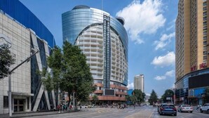 Een modern hotel met een gebogen glazen gevel, een opvallende ingang en een parkeerplaats met auto's.