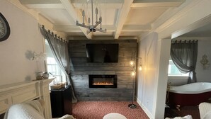 Una habitación con chimenea, dos sillones blancos, alfombra roja y una bañera.